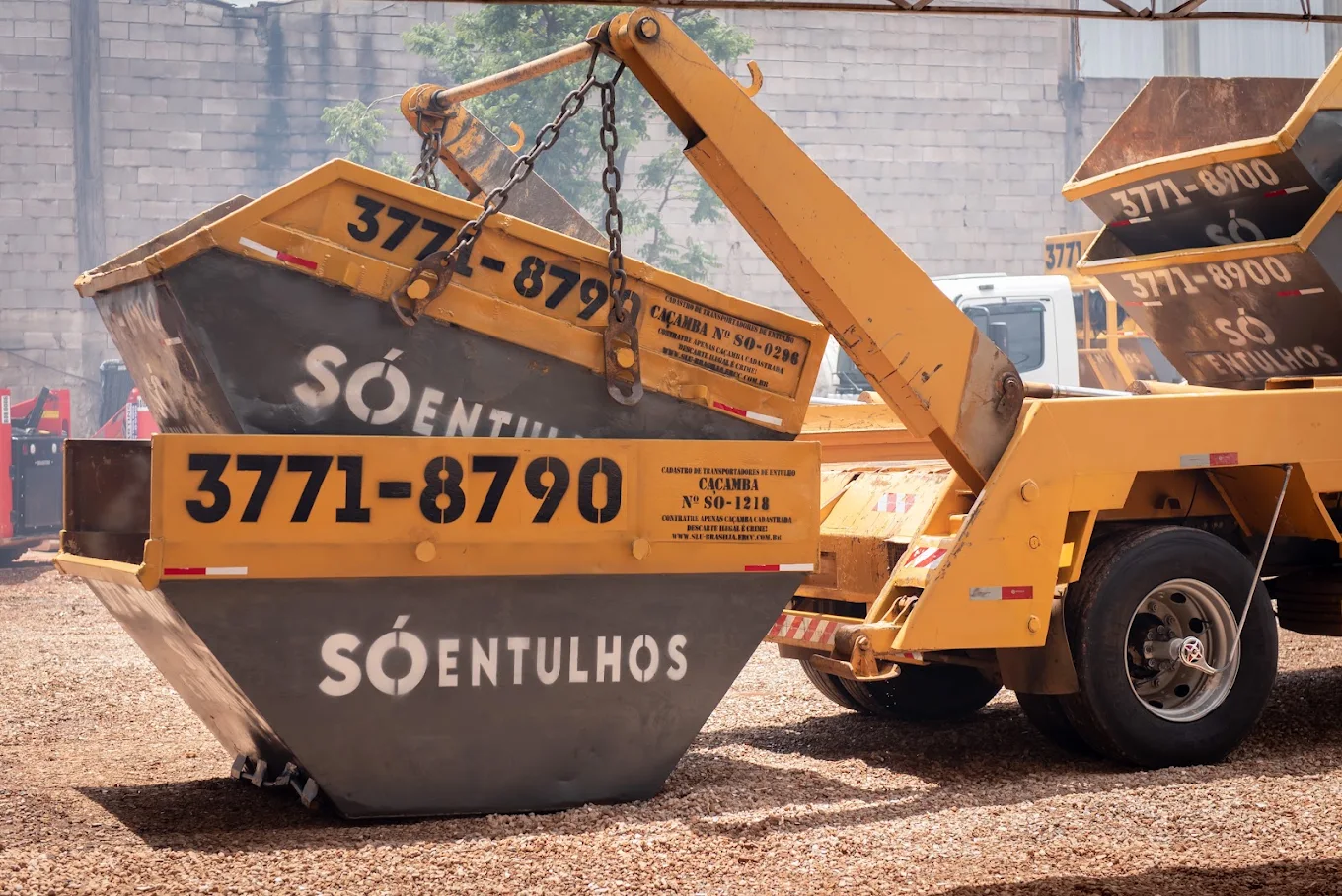 Caçamba de entulho Só Entulhos, cinza com borda amarela e telefone 3771-8790, em pátio industrial